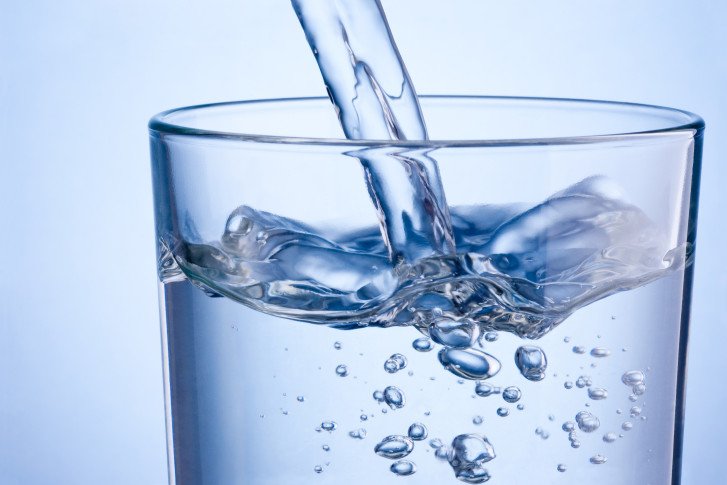 Close-up pouring water into glass on a blue background